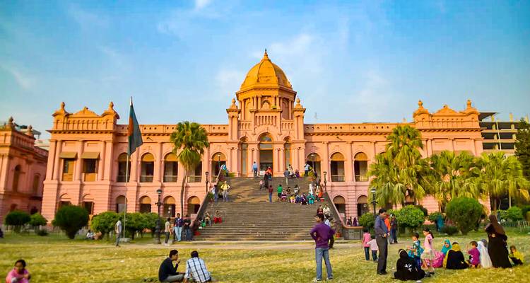 Large pink building with a dome, people sitting on grass.