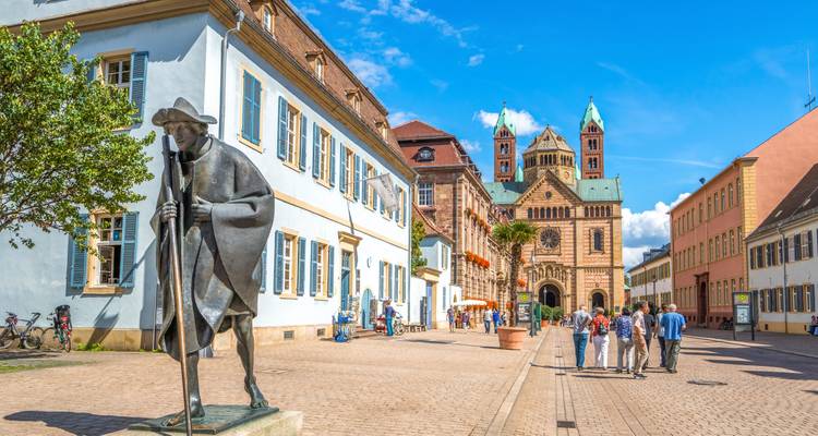 Pedestrian street with pilgrim statue leading to historic cathedral; tourists walk under bright summer skies.