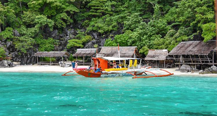 Botes tradicionales coloridos cerca de una playa de arena blanca y cabañas tropicales.