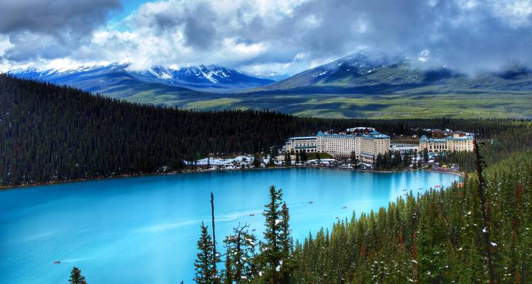Le lac Louise turquoise avec le grand Château Fairmont niché parmi les pics enneigés et la dense forêt de pins.