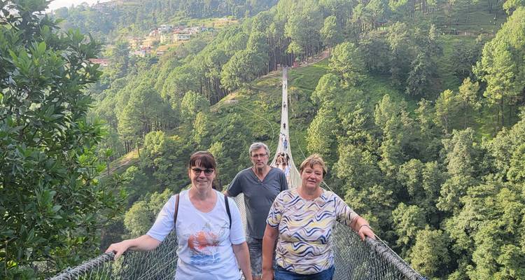 People walking across a suspension bridge with forested hills.
