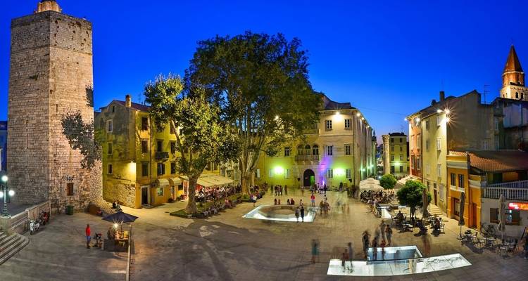 Place du village avec bâtiments éclairés au crépuscule.