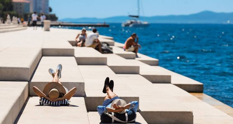 People laying on the steps by the sea enjoying the sunshine.