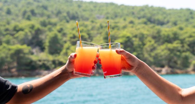 Hands holding tropical drinks with an ocean backdrop.