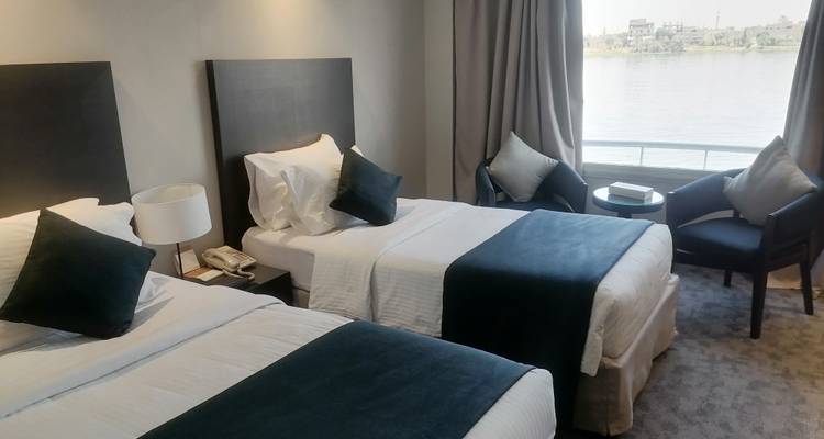 Zweibettzimmer-Kreuzfahrtkabine mit Flussblick durch ein Fenster.