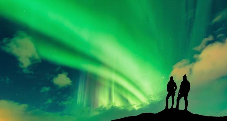 Deux personnes en silhouette contre les aurores boréales dans le ciel nocturne.