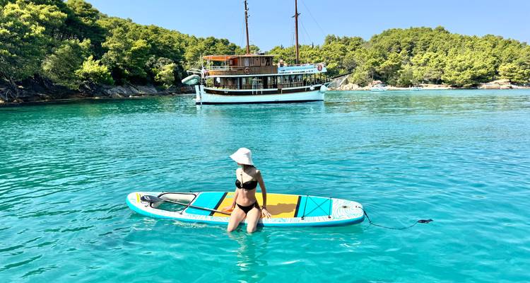Personne sur une planche à pagaie dans une eau turquoise claire avec un bateau au loin.