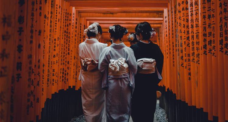 Three women in traditional kimonos walking through Fushimi Inari Shrine in Kyoto, Japan.