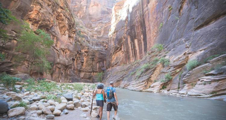 Excursionistas caminando por un cañón con acantilados imponentes en el Parque Nacional Zion.