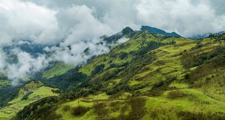 Exuberantes colinas ondulantes andinas cubiertas de pastos esmeralda con nubes bajas aferradas a las crestas