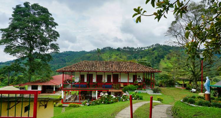 Casa tradicional de finca cafetera con balcones rojos situada entre colinas verdes en un día nublado
