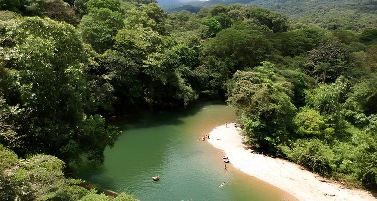 Aerial view of a green jungle river bend with swimmers enjoying a sandy riverbank beach.