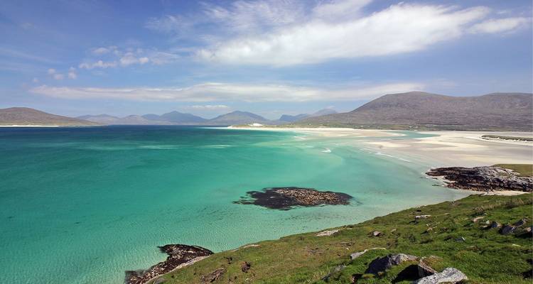 Baie d'un turquoise spectaculaire avec des plages de sable blanc et des montagnes écossaises lointaines