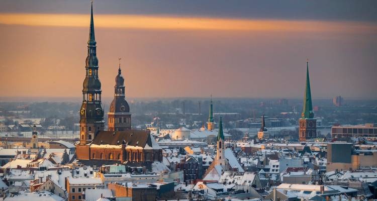Horizonte cubierto de nieve de Riga al amanecer con icónicos campanarios elevándose sobre los tejados históricos.