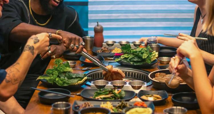 Les amis grillent de la viande et des légumes sur une table de barbecue coréen intégrée, entourée de plats d'accompagnement colorés.