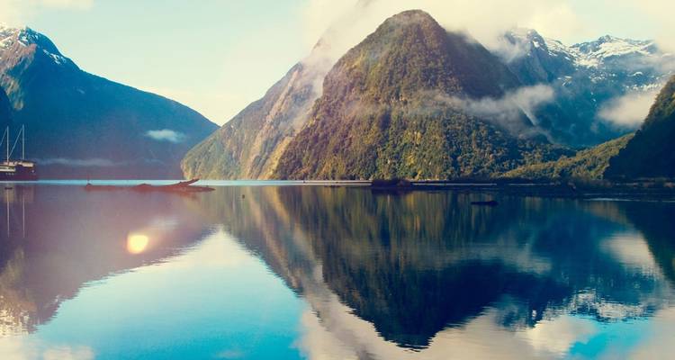 Un fjord serein reflète les montagnes enveloppées de brume avec une lumière matinale douce créant une atmosphère tranquille.