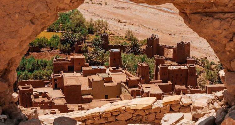 Bâtiments de forteresse marocaine traditionnelle vus à travers une fenêtre voûtée en pierre.