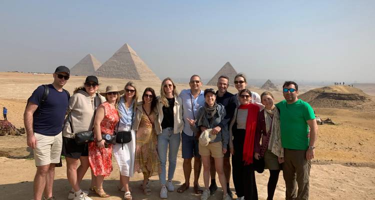 Gran grupo turístico sonríe frente al panorama de la pirámide en el desierto de Giza.