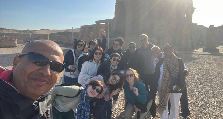 Grote toergroep die hurkt en zwaait voor een selfie bij Egyptische ruïnes in ochtendzonlicht van achteren