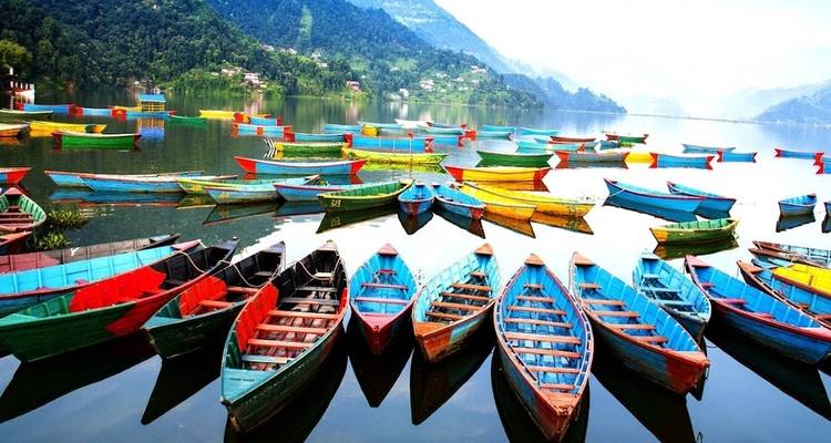 Kleurrijke roeiboten op een meer met bergachtige achtergrond.