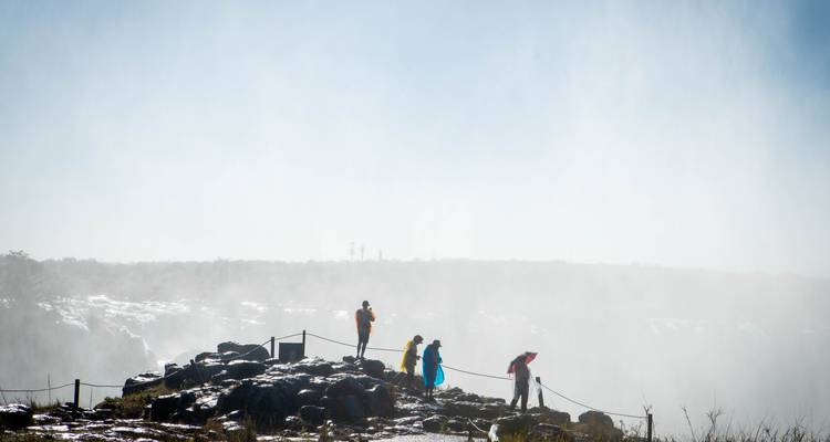 Visitors in bright ponchos viewing a mist-covered waterfall.
