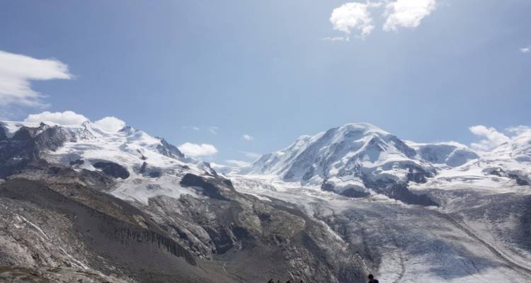 Besneeuwde bergketen met heldere blauwe lucht en een paar mensen onderaan.