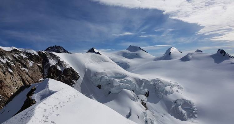 Sneeuwbedekte bergtoppen en rollende wolken onder een levendige hemel.
