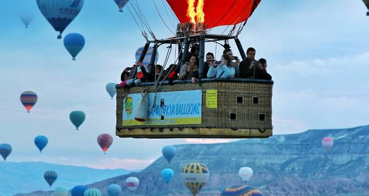 Hot air balloon with people rising in a sky filled with balloons.