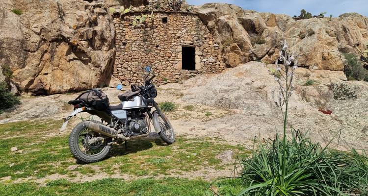 Motorcycle parked by a rocky structure in an arid area.