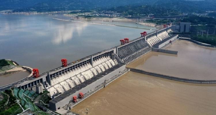 Large dam across a river with lush mountainous backdrop.