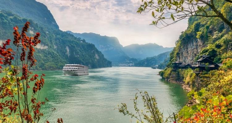 Cruise ship sailing through a river surrounded by mountainous landscape.