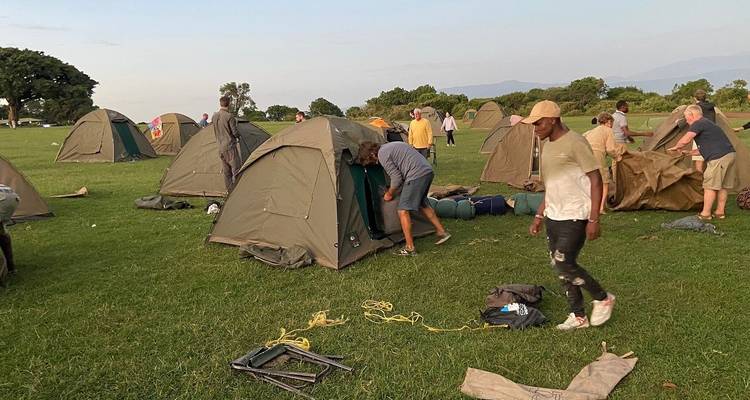 Group setting up tents on a green field with mountains.