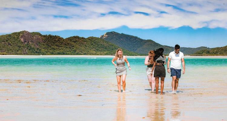 People walking on a scenic beach with clear water.
