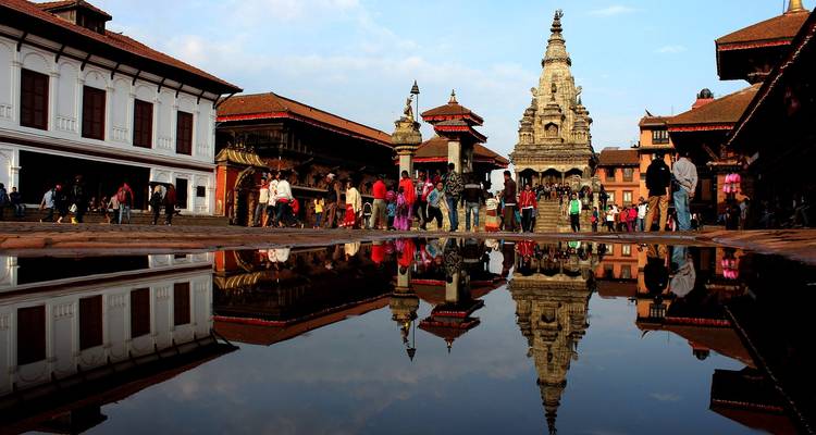 Reflet d'un temple et de personnes dans une flaque d'eau.