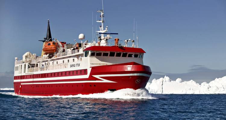 Barco rojo y blanco navegando por aguas heladas con icebergs.