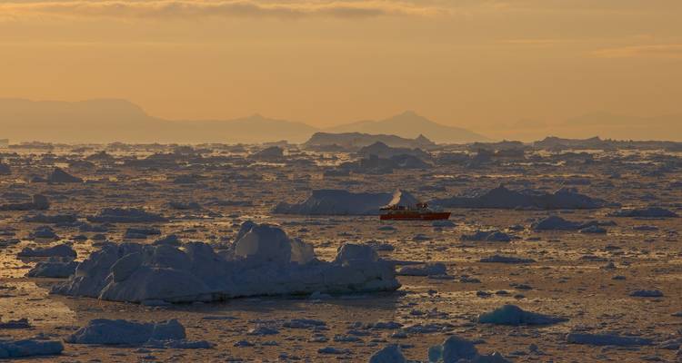 Mar salpicado de icebergs al atardecer con montañas distantes.