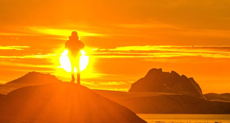 Silueta de una persona en una colina contra una puesta de sol vívida.