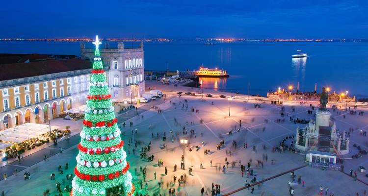 Nighttime view of Lisbon’s Praça do Comércio with a giant illuminated Christmas tree and waterfront lights.