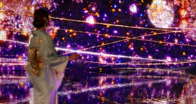 Persoon in traditionele kledij die naar een lichtinstallatie kijkt.