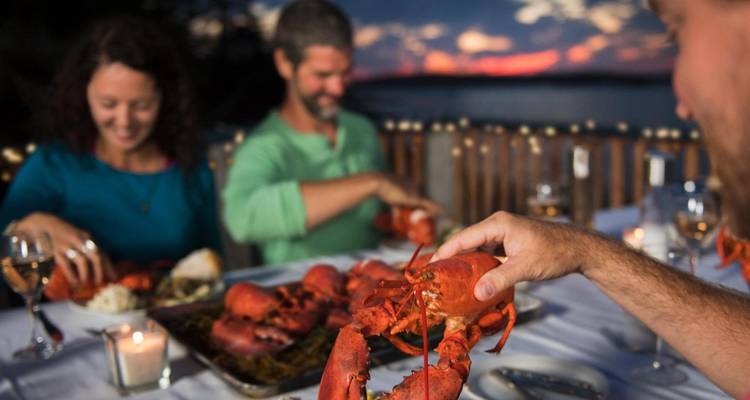 Menschen, die ein Hummer-Dinner am Wasser bei Sonnenuntergang genießen.