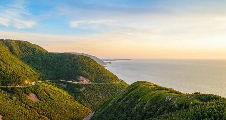 Malerische Aussicht auf üppig grüne Hügel und Ozean bei Sonnenuntergang.
