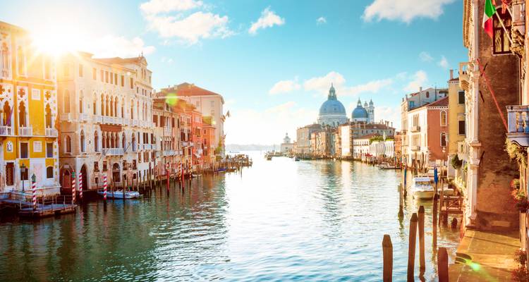 Le Grand Canal bordé de palais ornés brillant sous le soleil du matin avec une basilique à dôme au loin.