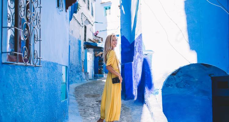 Une personne en robe jaune marchant dans une rue peinte en bleu.