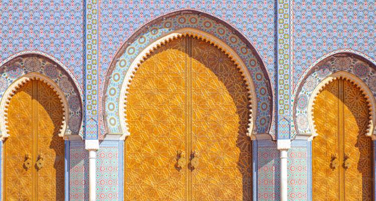 Gros plan de trois portes dorées géantes encadrées par un carrelage géométrique coloré et des arcs en pierre sculptée.