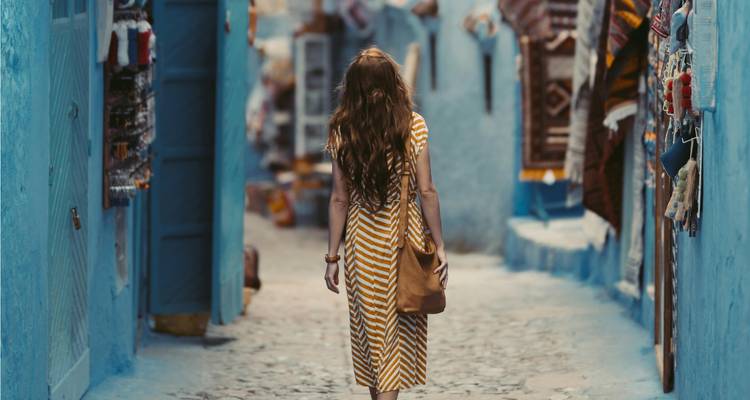 Une femme en robe rayée se promène dans une ruelle bleue étroite bordée d'étals d'artisans.