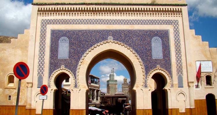 Das verzierte Blaue Tor mit kunstvollen Kacheln und dreifachen Bögen rahmt einen Blick auf eine alte Medina-Straße dahinter ein.