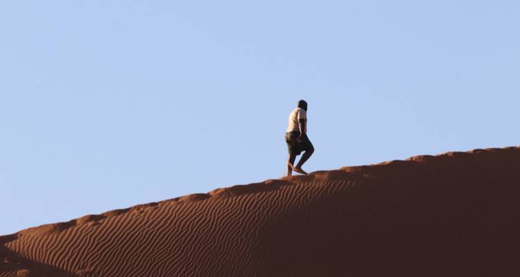 Person, die auf Sanddünen unter klarem Himmel wandelt.