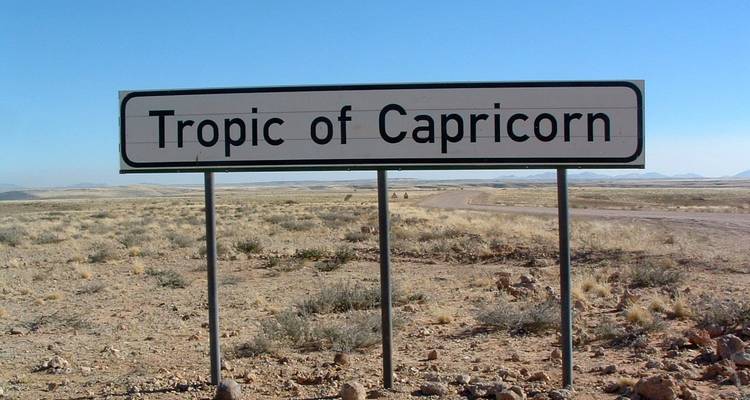 Ein Schild, das den Wendekreis des Steinbocks in einer Wüstenlandschaft anzeigt.