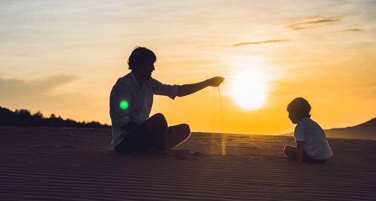 Silueta de un padre e hijo jugando con arena durante el atardecer.