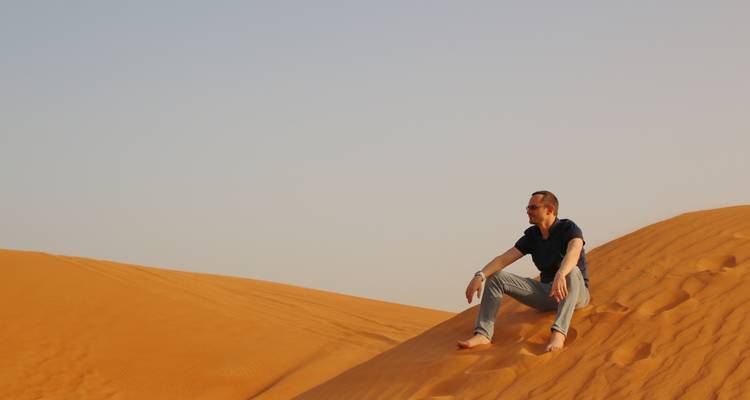 Homme assis sur une dune de sable admirant le paysage désertique.
